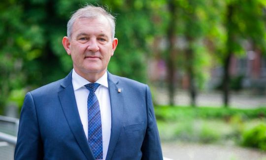 Zdjęcie portretowe. Prof. dr hab. inż. Krzysztof Jóźwik w niebieskim garniturze, białej koszuli i krawacie. W tle zieleń drzew kampusu PŁ.