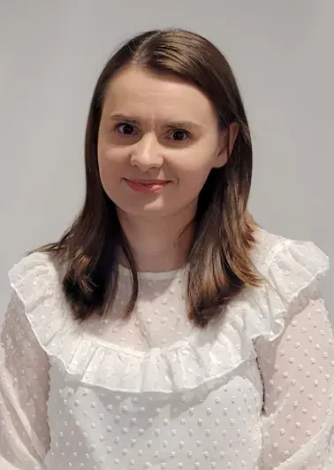 portret uśmiechniętej młodej kobiety z brązowymi włosami, w białej bluzce z falbanką
