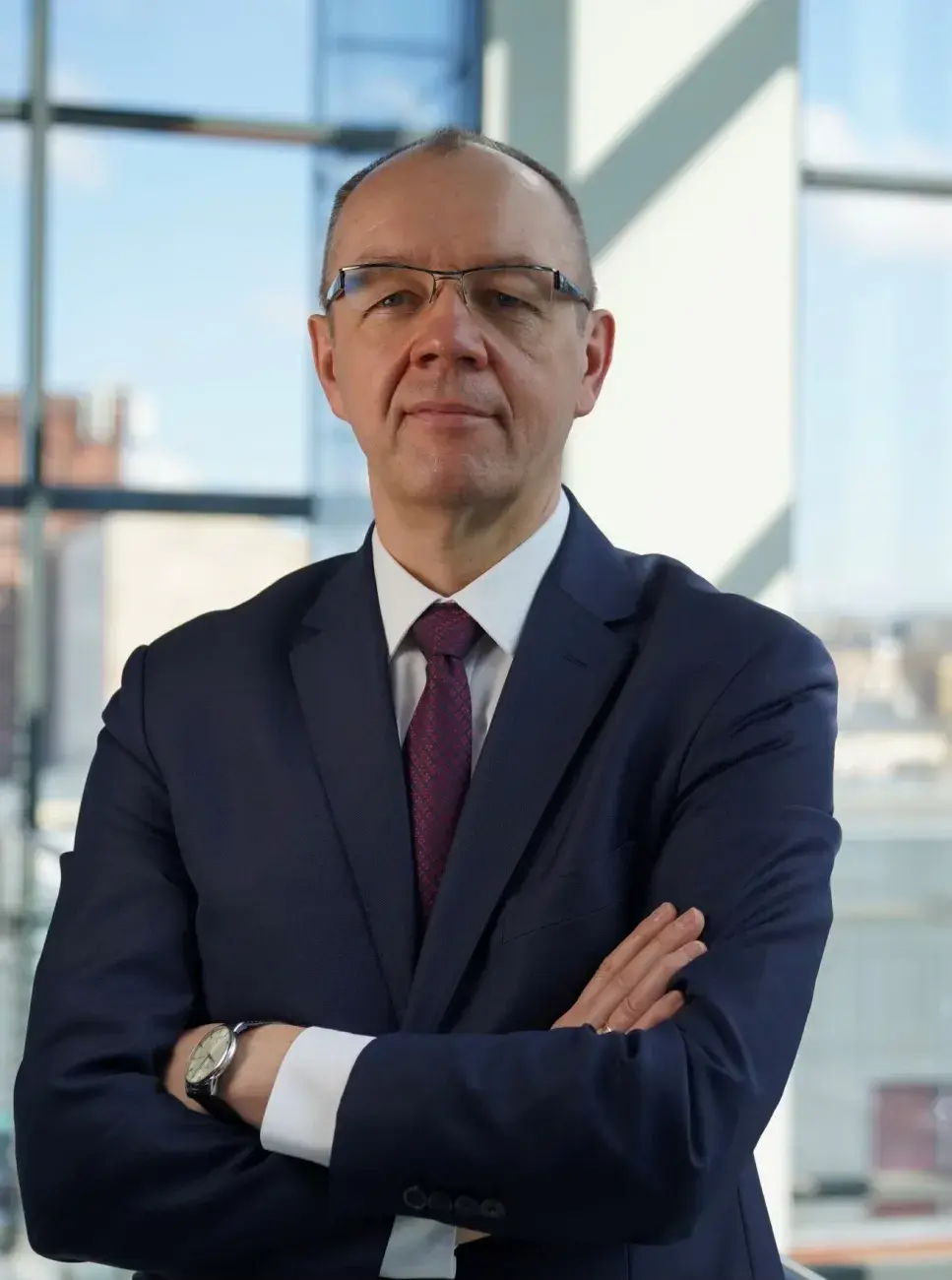 portret mężczyzny w średnim wieku, w garniturze, z założonymi rękoma, w okularach, w tle przeszklona ściana
