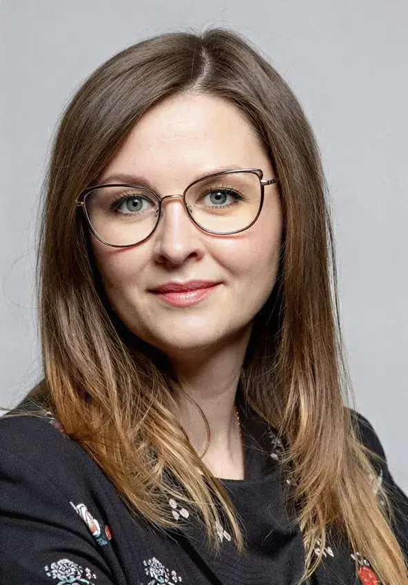 zdjęcie portretowe młodej kobiety w okularach, włosach do ramion, uśmiecha się, tło szare