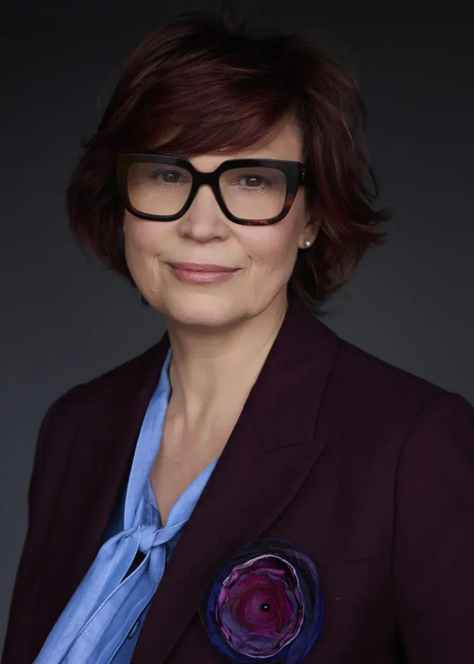 portret uśmiechniętej kobiety w okularach, ciemne tło, ciemna marynarka, błękitna bluzka, prof. Edyta Gendaszewska-Darmach