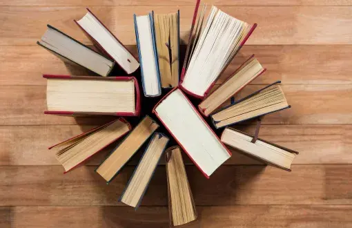 Photo from above: a dozen books stacked vertically on a wooden floor.