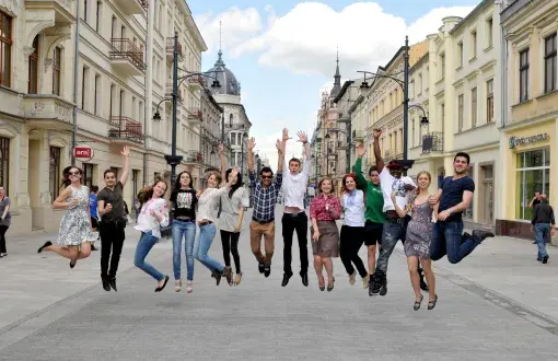 14 zagranicznych studentów uchwyconych w podskoku na ul. Piotrkowskiej w słoneczny dzień.