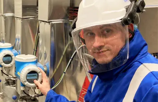 Maciej Komorowski przy stanowisku pomiarowym w białym kasku z przyłbicą i niebieskim skafandrze w laboratorium Contec Poland.