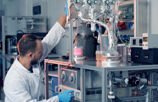 Prof. Jacek Tyczkowski w białym fartuchu w laboratorium, przy specjalistycznym urządzeniu.