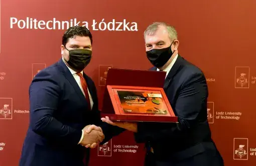 Rektor prof. Krzysztof Jóźwi0k odbiera gratulacje od prezesa Polskiej Agencji Przedsiębiorczości Wojciecha Pomarańskiego. Uścisk dłoni. JM Rektor trzyma pamiątkową tabliczkę w bordowym etui.