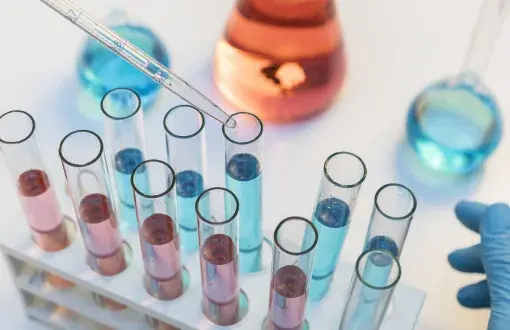 Kilkanaście różnokolorowych probówek na stole laboratoryjnym.