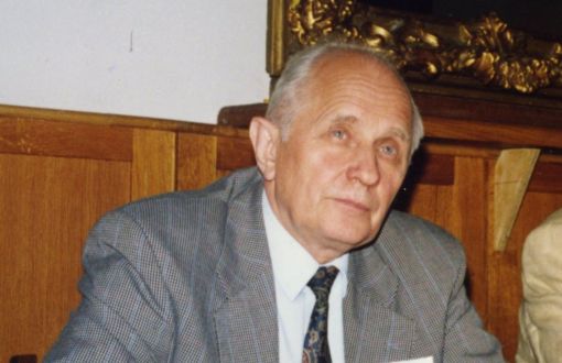 prof. Czesław Strumiłło w jasnym garniturze siedzi przy drewnianym stole.