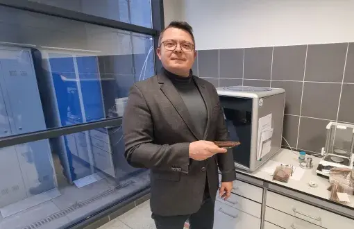 Dr inż. Adam Szufa w garniturze przy stanowisku laboratoryjnym.