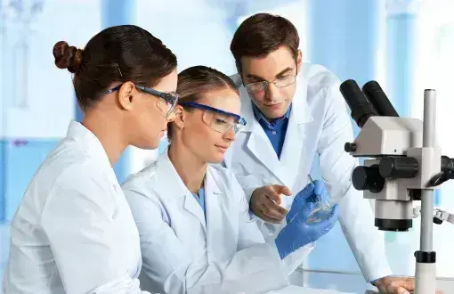 Troje laborantów w białych fartuchach siedzi przy mikroskopie.