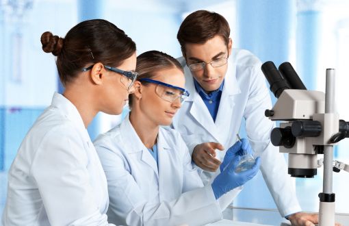 Troje laborantów w białych fartuchach siedzi przy mikroskopie.
