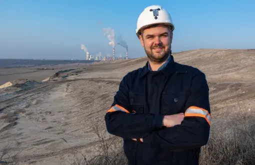 Damian Kądrowski w kasku na tle wykopalisk.