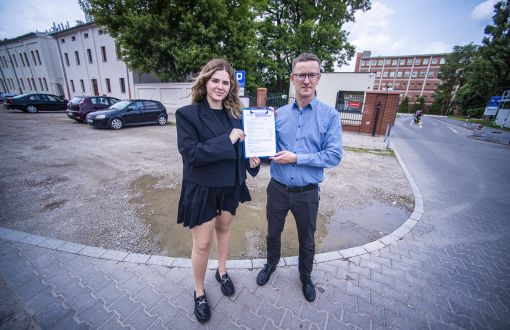 kobieta i mężczyzna stoją trzymając dokumentwprost do obiektywu, w tle kałuża