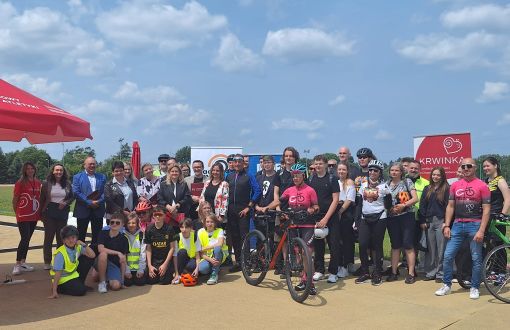 grupa rowerzystów pozuje do zdjęcia, ludzie uśmiechnięci w tle błękitne niebo i obłoki