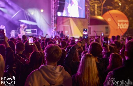 grupa młodych ludzi stojących tyłem do obiektywu, bawiących się na plenerowym koncercie