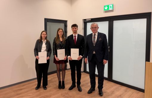 Troje młodych osób z dyplomami w rękach stoi w towarzystwie eleganko ubranego mężczyzny