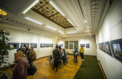 wnętrze zabytkowego budynku, zdobiony sufit, parkietowa podłoga, na ścianach obrazy, po środku kilka osób zwiedzających