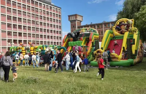 dmuchańce gumowe kolorowe przy których stoją dzieci i dorośli, w tle ceglany zabudowania, błękitne niebo