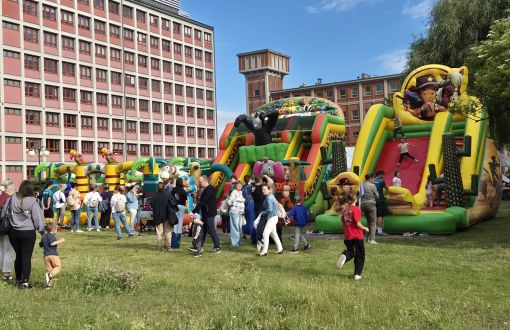 dmuchańce gumowe kolorowe przy których stoją dzieci i dorośli, w tle ceglany zabudowania, błękitne niebo