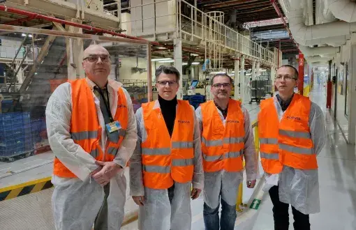 Czterech mężczyzn w jaskrawych kamizelkach na tle linii produkcyjnej