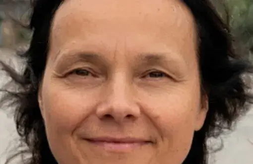 portret kobiety uśmiechniętej, ciemne rozwiane włosy, w tle krajobraz naturalny
